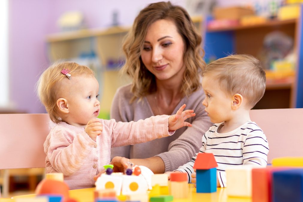 Babies with mentor in kindergarten. Kids toddlers in nursery school. Little girl and boy preschoolers playing with teacher.